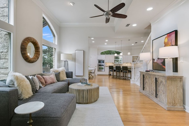 living room with light wood finished floors, visible vents, a towering ceiling, stairway, and ornamental molding