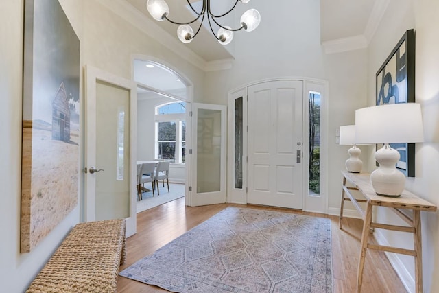 entryway with a notable chandelier, wood finished floors, and crown molding