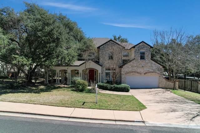 french provincial home with a garage, fence, stone siding, concrete driveway, and a front lawn