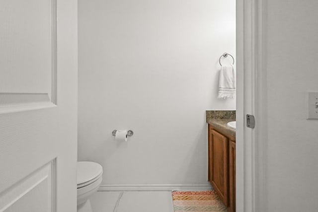 half bath with toilet, tile patterned floors, vanity, and baseboards