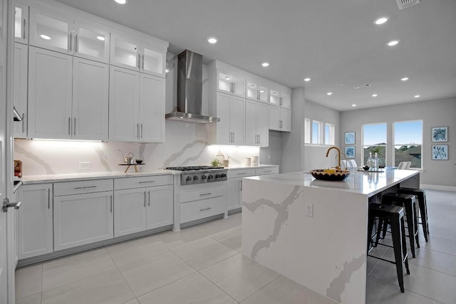 kitchen with an island with sink, recessed lighting, wall chimney exhaust hood, white cabinets, and stainless steel gas cooktop