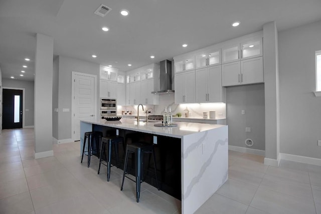 kitchen with visible vents, white cabinetry, recessed lighting, wall chimney range hood, and glass insert cabinets