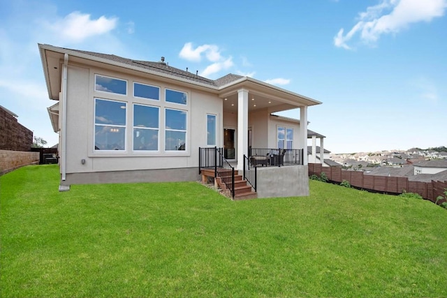 back of house with stucco siding, a lawn, and fence