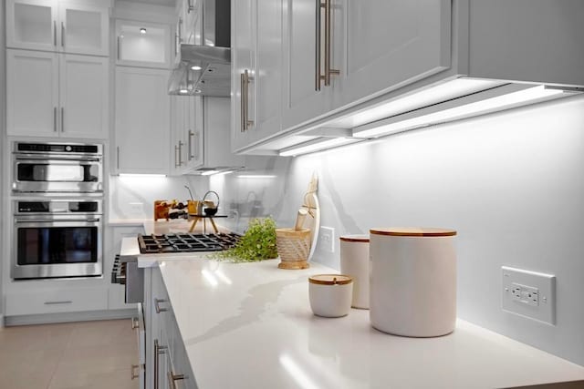16909 Roselin Dr, Austin, TX 78738 - kitchen featuring light countertops, stainless steel double oven, glass insert cabinets, wall chimney range hood, and white cabinets