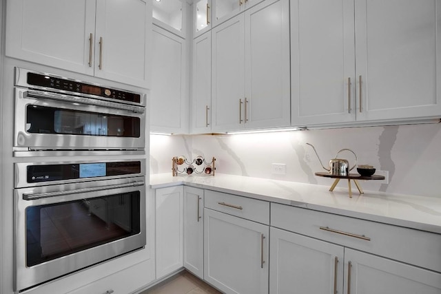 kitchen featuring double oven, white cabinets, glass insert cabinets, and light stone countertops