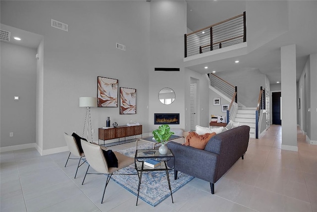 living area featuring visible vents, baseboards, a glass covered fireplace, and stairs