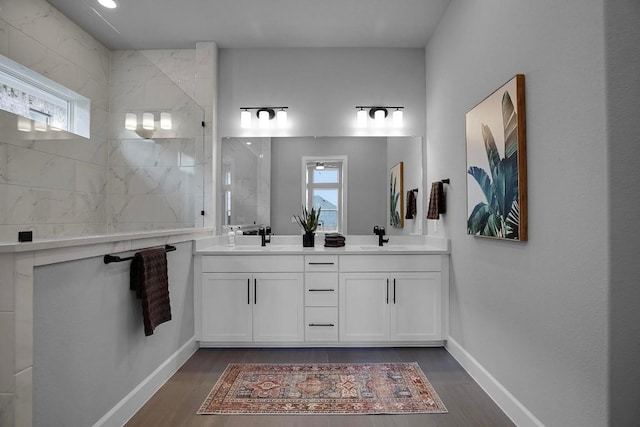 full bathroom featuring wood finished floors, baseboards, double vanity, a sink, and a walk in shower