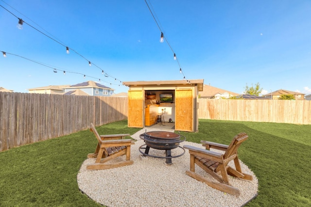 view of yard featuring an outdoor fire pit, a storage unit, a fenced backyard, and an outbuilding