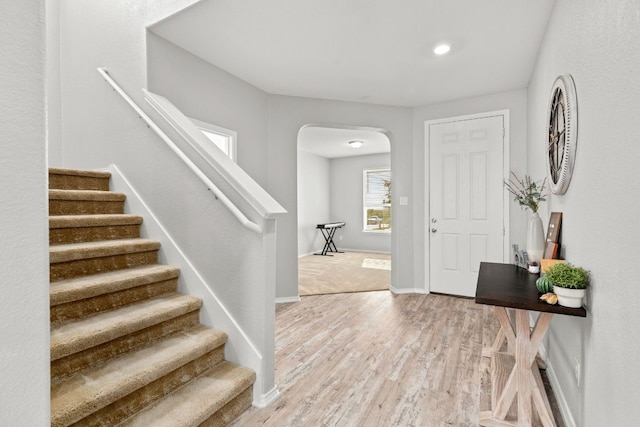 entrance foyer with light wood finished floors, baseboards, stairs, and arched walkways