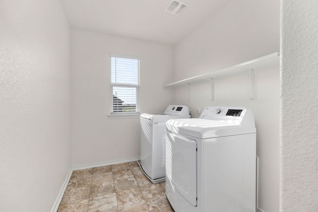 washroom featuring laundry area, separate washer and dryer, visible vents, baseboards, and stone finish floor