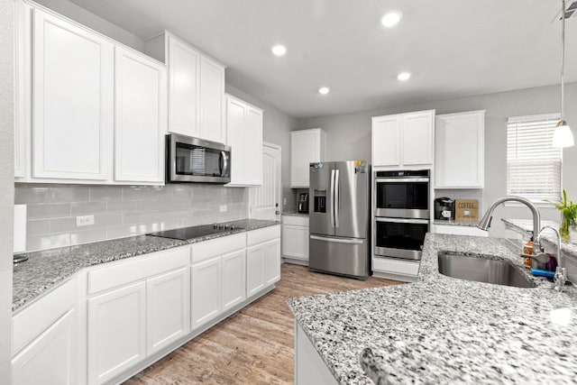 kitchen with light wood-style flooring, a sink, white cabinets, appliances with stainless steel finishes, and decorative backsplash