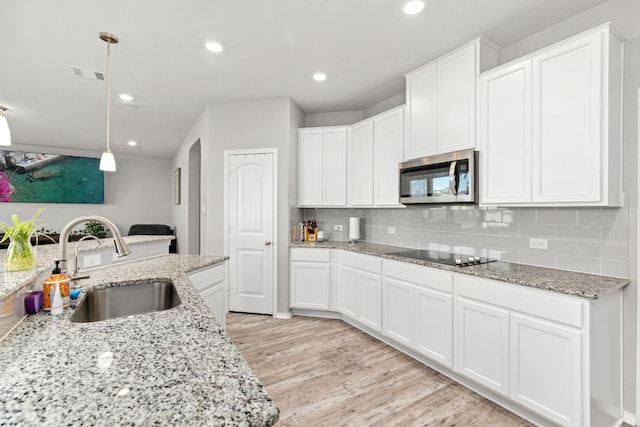 kitchen featuring black electric stovetop, a sink, visible vents, decorative backsplash, and stainless steel microwave