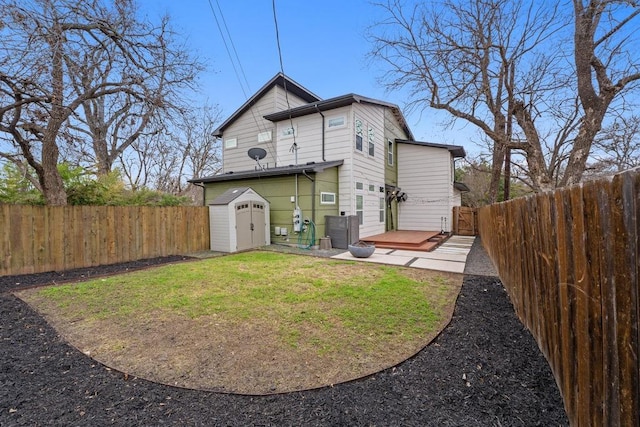 rear view of property featuring a deck, a lawn, an outbuilding, and a fenced backyard