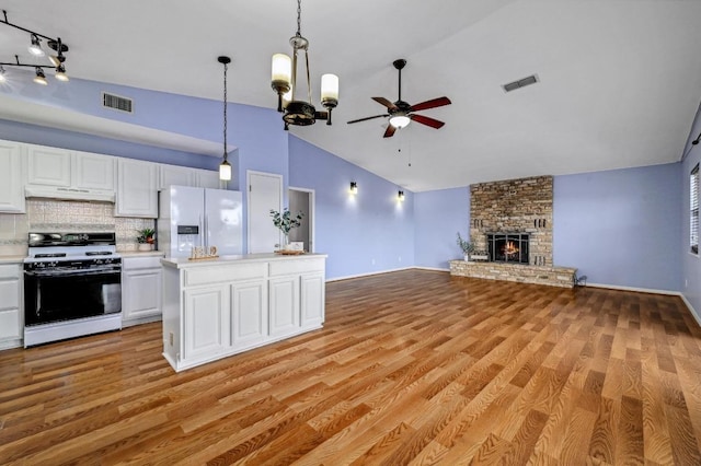 kitchen with under cabinet range hood, visible vents, range with gas stovetop, and refrigerator with ice dispenser