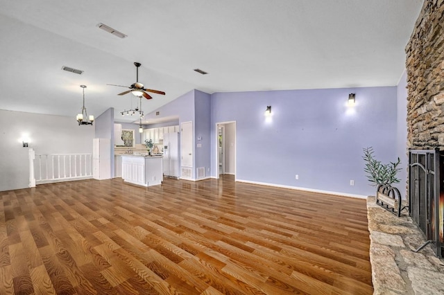 unfurnished living room with vaulted ceiling, ceiling fan with notable chandelier, a fireplace, and wood finished floors