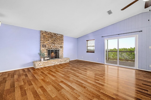 unfurnished living room with visible vents, vaulted ceiling, a stone fireplace, wood finished floors, and a ceiling fan