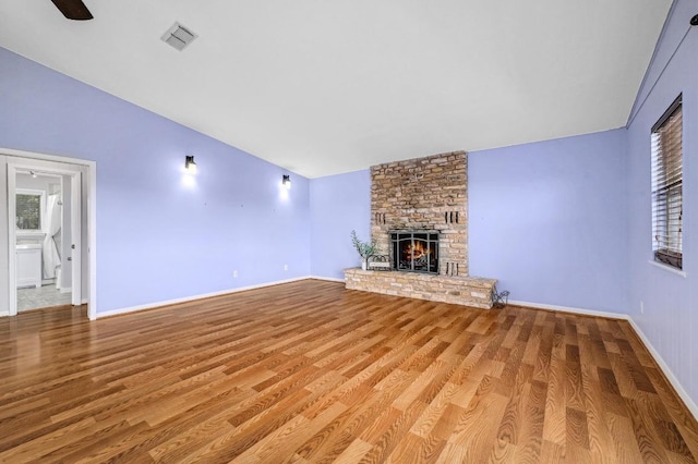 unfurnished living room featuring visible vents, a large fireplace, baseboards, lofted ceiling, and wood finished floors