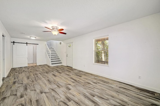 unfurnished living room featuring wood finished floors, baseboards, ceiling fan, stairs, and a barn door