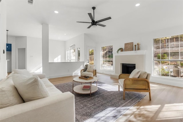 living area with recessed lighting, plenty of natural light, a fireplace with raised hearth, and light wood-style flooring