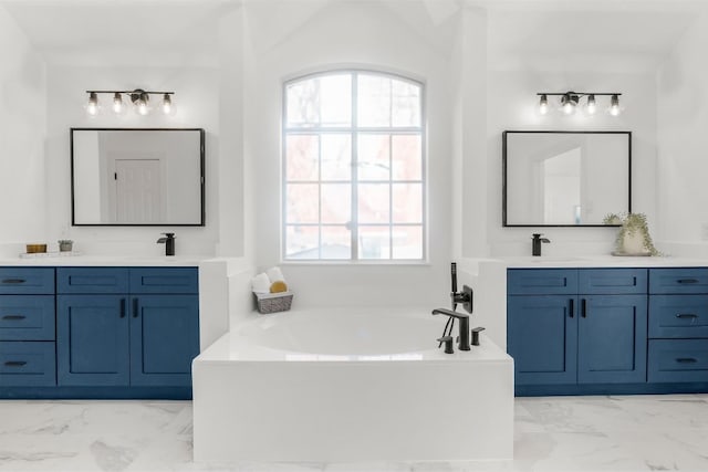 bathroom featuring marble finish floor, two vanities, a sink, and a bath