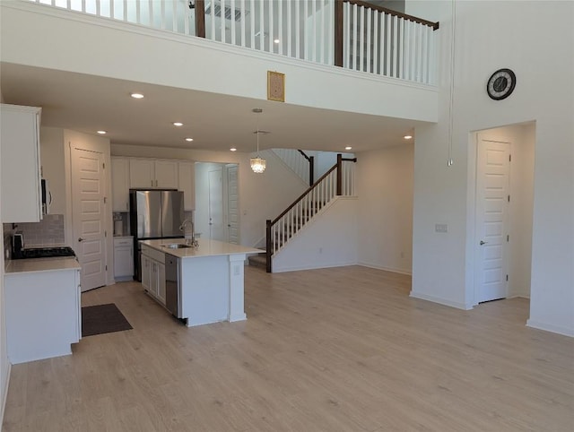 kitchen with stainless steel appliances, baseboards, white cabinets, hanging light fixtures, and light wood-type flooring