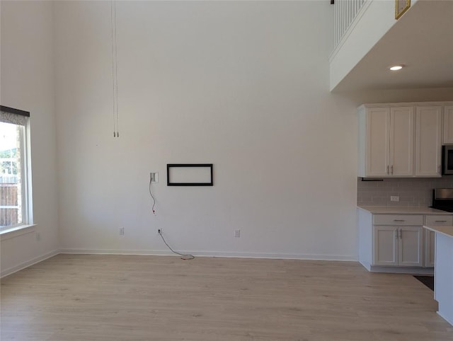 kitchen featuring tasteful backsplash, stainless steel microwave, a towering ceiling, and light wood finished floors