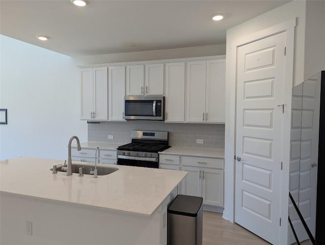 kitchen with tasteful backsplash, appliances with stainless steel finishes, light stone counters, white cabinetry, and a sink