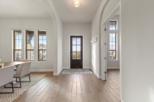 entrance foyer with baseboards, arched walkways, and wood finished floors