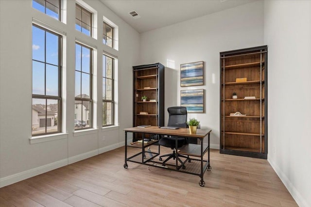 home office featuring a healthy amount of sunlight, visible vents, light wood-style flooring, and baseboards