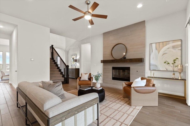 living area with ceiling fan, a tile fireplace, wood finished floors, baseboards, and stairs