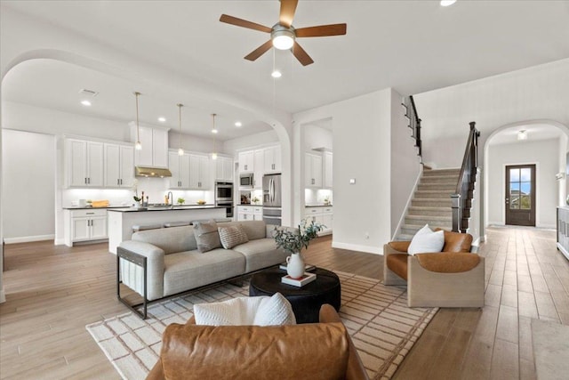 living area with arched walkways, light wood-type flooring, stairs, and baseboards