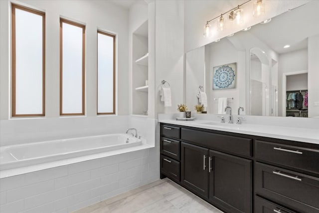 full bathroom featuring a walk in closet, vanity, and a bath