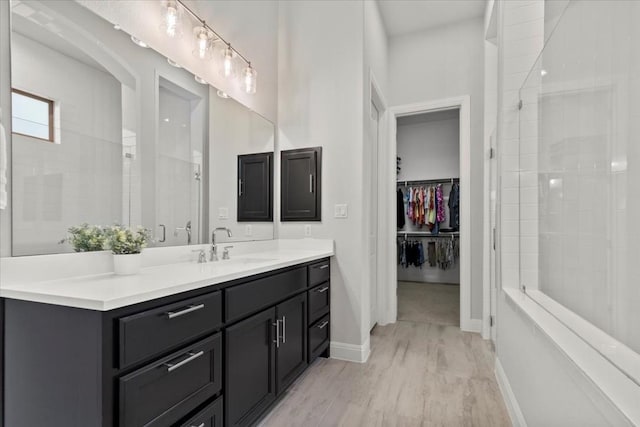 bathroom featuring a walk in closet, a tile shower, vanity, and baseboards