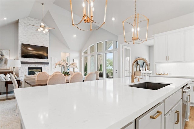 kitchen with a fireplace, a center island with sink, light countertops, white cabinets, and a sink