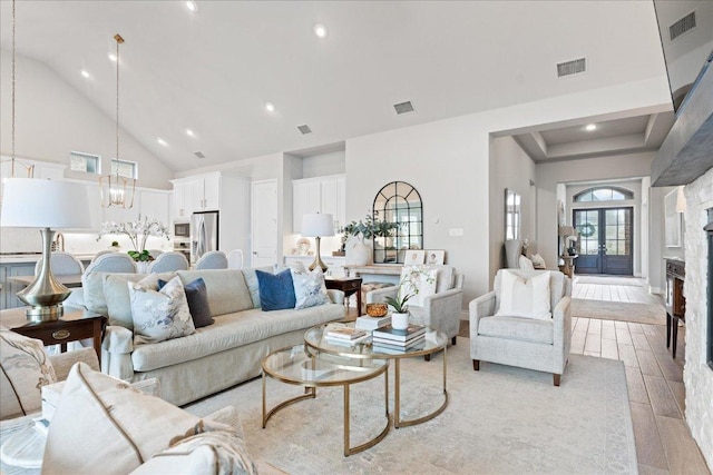 living area with high vaulted ceiling, visible vents, a notable chandelier, and light wood-style flooring