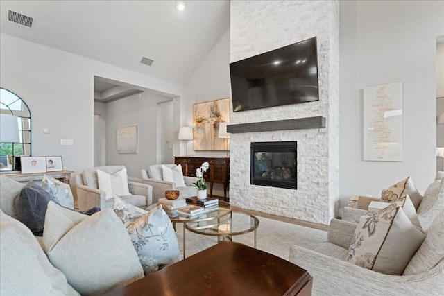 living room featuring high vaulted ceiling, visible vents, a stone fireplace, and wood finished floors