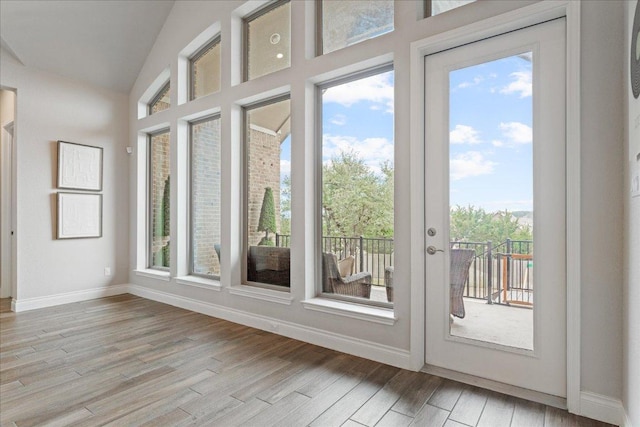 doorway with light wood-type flooring, lofted ceiling, and baseboards