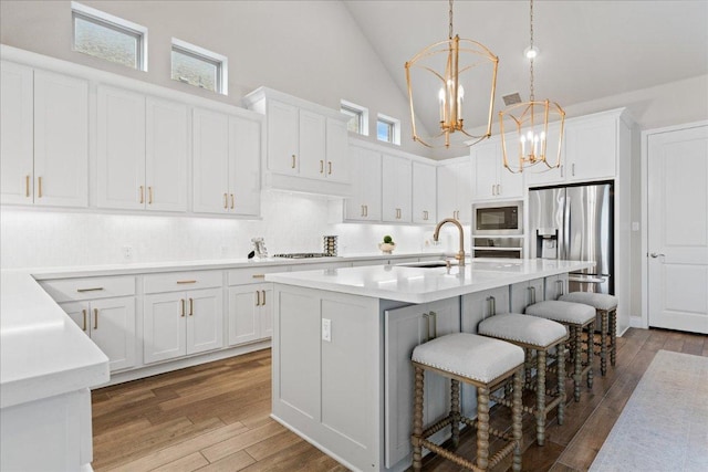 kitchen featuring a notable chandelier, wood finished floors, a sink, appliances with stainless steel finishes, and a kitchen bar