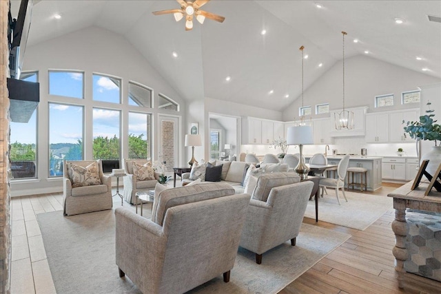 living area with ceiling fan with notable chandelier, high vaulted ceiling, light wood-type flooring, and visible vents