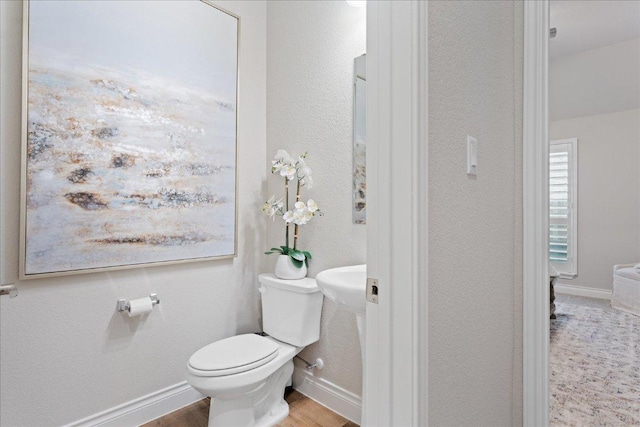 half bathroom featuring wood finished floors, toilet, and baseboards