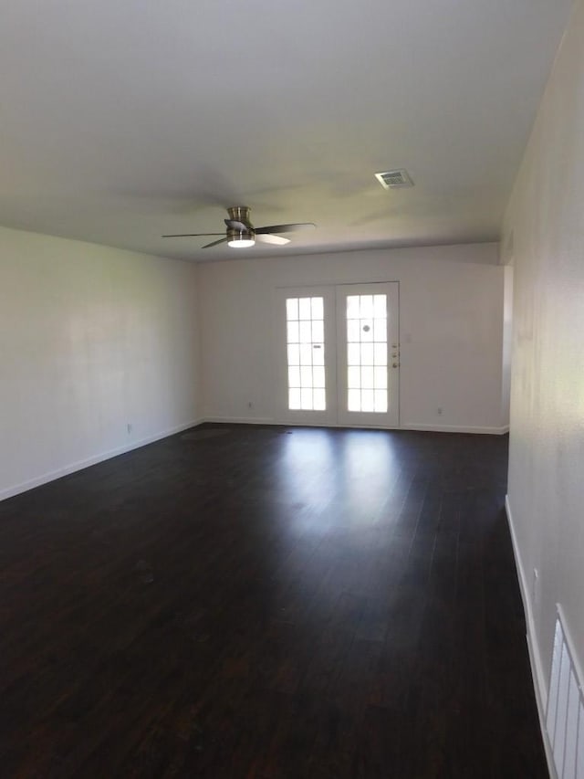 empty room featuring a ceiling fan, dark wood finished floors, visible vents, and baseboards