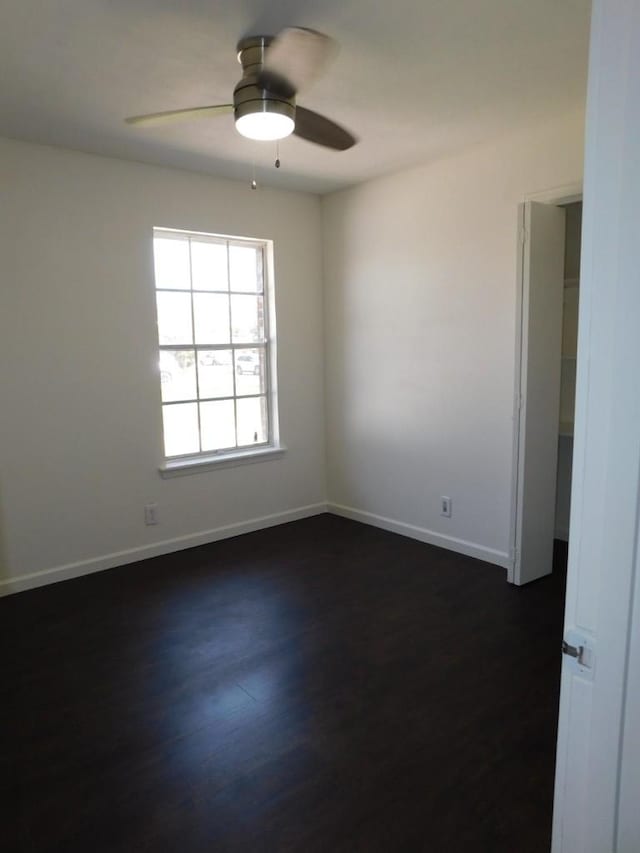 empty room with baseboards, dark wood finished floors, and a ceiling fan