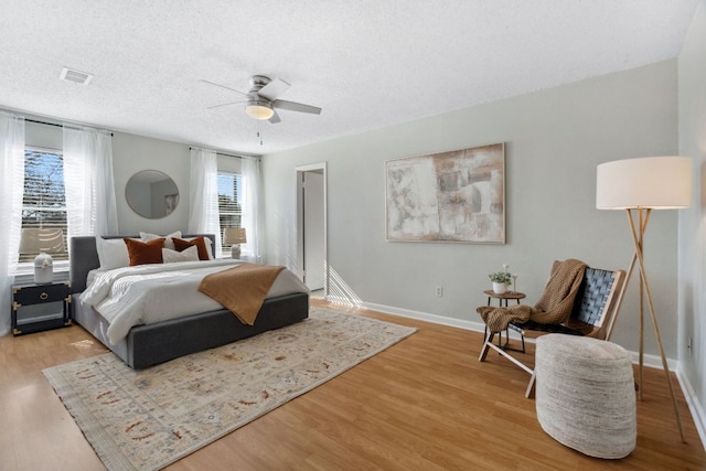 bedroom with a textured ceiling, ceiling fan, wood finished floors, visible vents, and baseboards