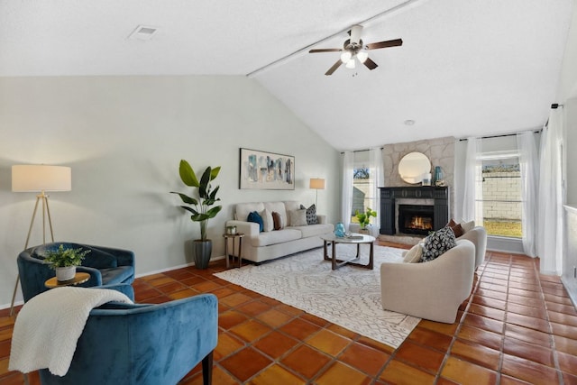 tiled living area featuring vaulted ceiling, a stone fireplace, a ceiling fan, and baseboards