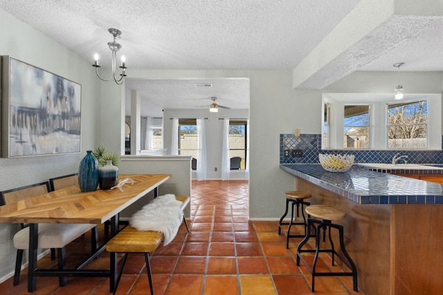 tiled dining room featuring ceiling fan with notable chandelier, a textured ceiling, a sink, and baseboards