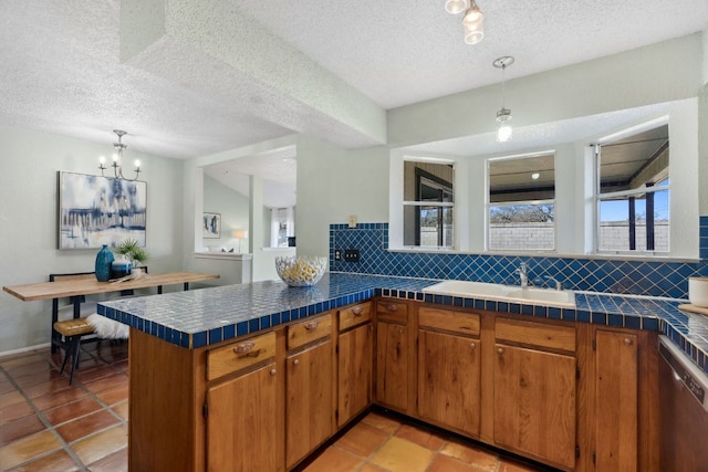 kitchen with brown cabinetry, dishwasher, a peninsula, a sink, and backsplash