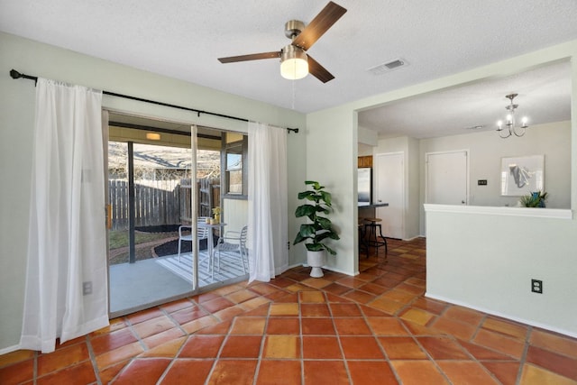 empty room featuring a textured ceiling, ceiling fan with notable chandelier, tile patterned flooring, and visible vents