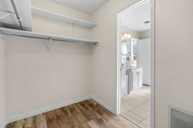 spacious closet with light wood-style floors, visible vents, and a sink