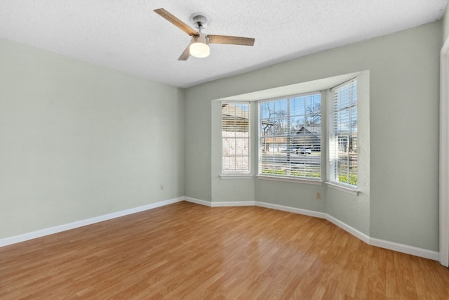 empty room with light wood-style flooring, baseboards, ceiling fan, and a textured ceiling