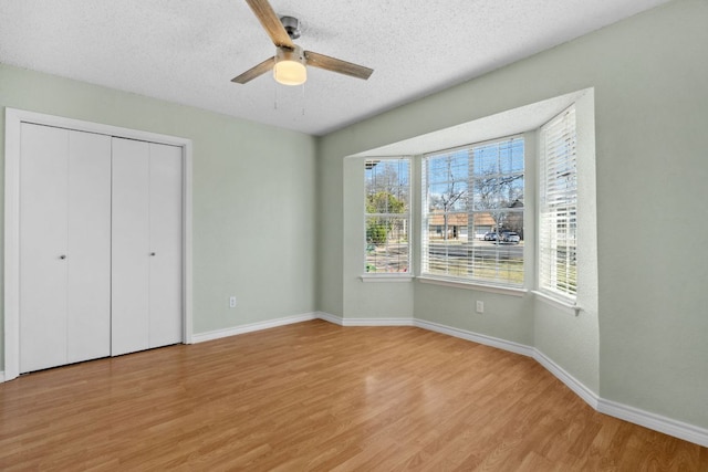 unfurnished bedroom featuring a textured ceiling, a ceiling fan, baseboards, light wood-style floors, and a closet